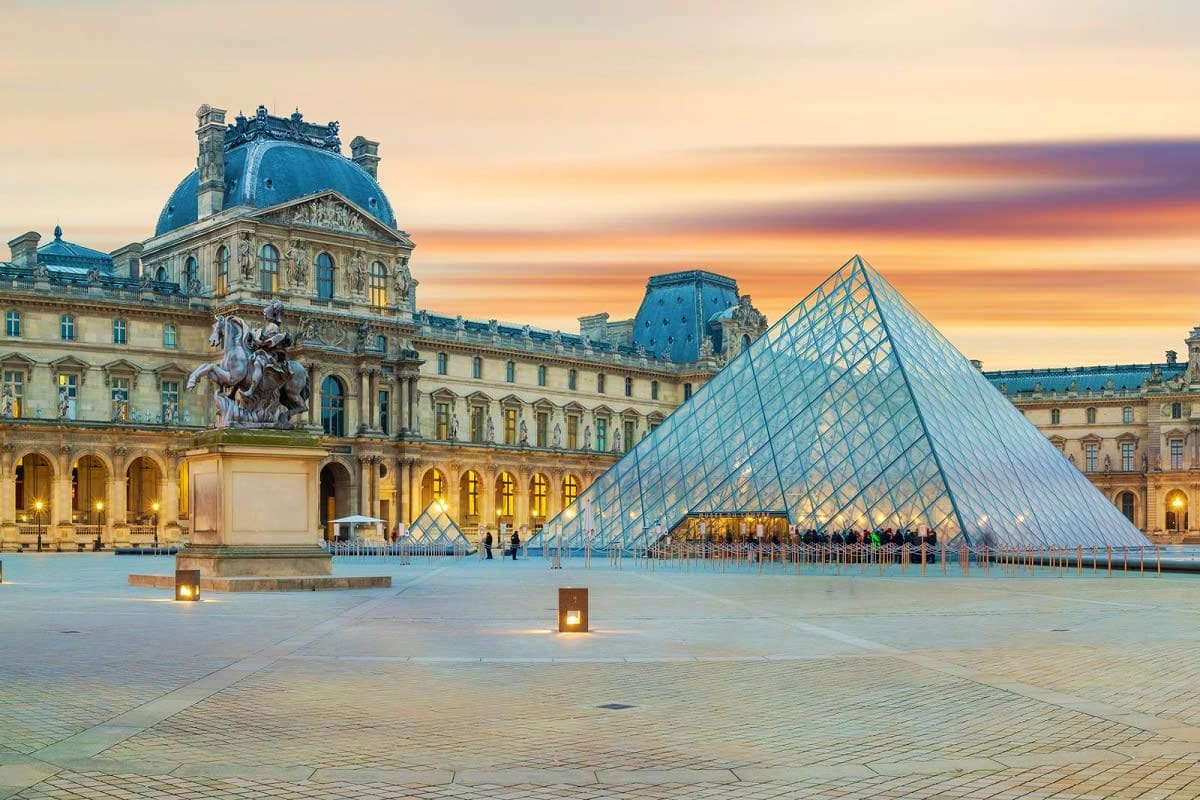 Louvre Museum with glass pyramid and palace courtyard at sunset in Paris, France