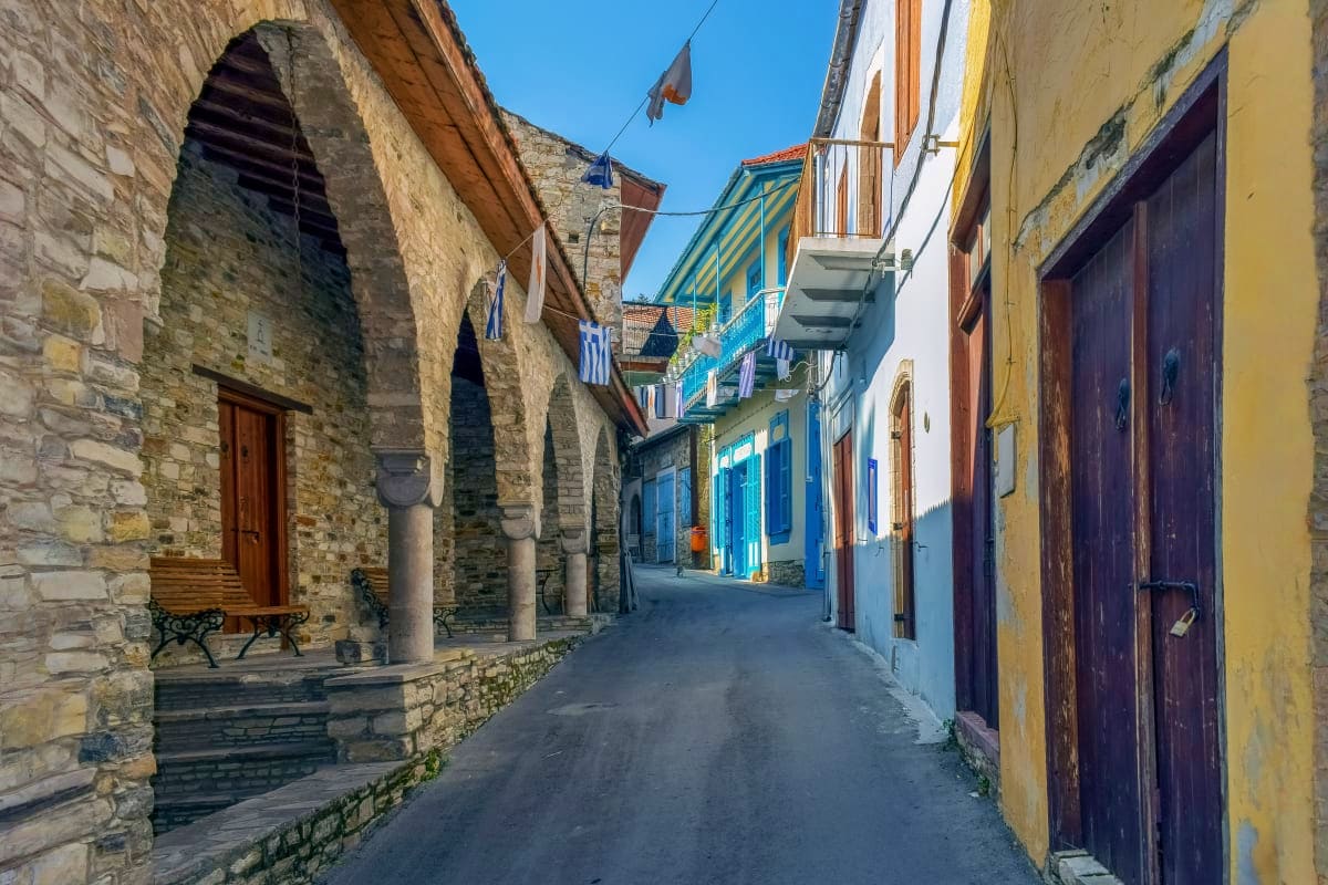 Narrow cobblestone street in traditional Cypriot village with stone buildings, blue shutters, and arched doorway