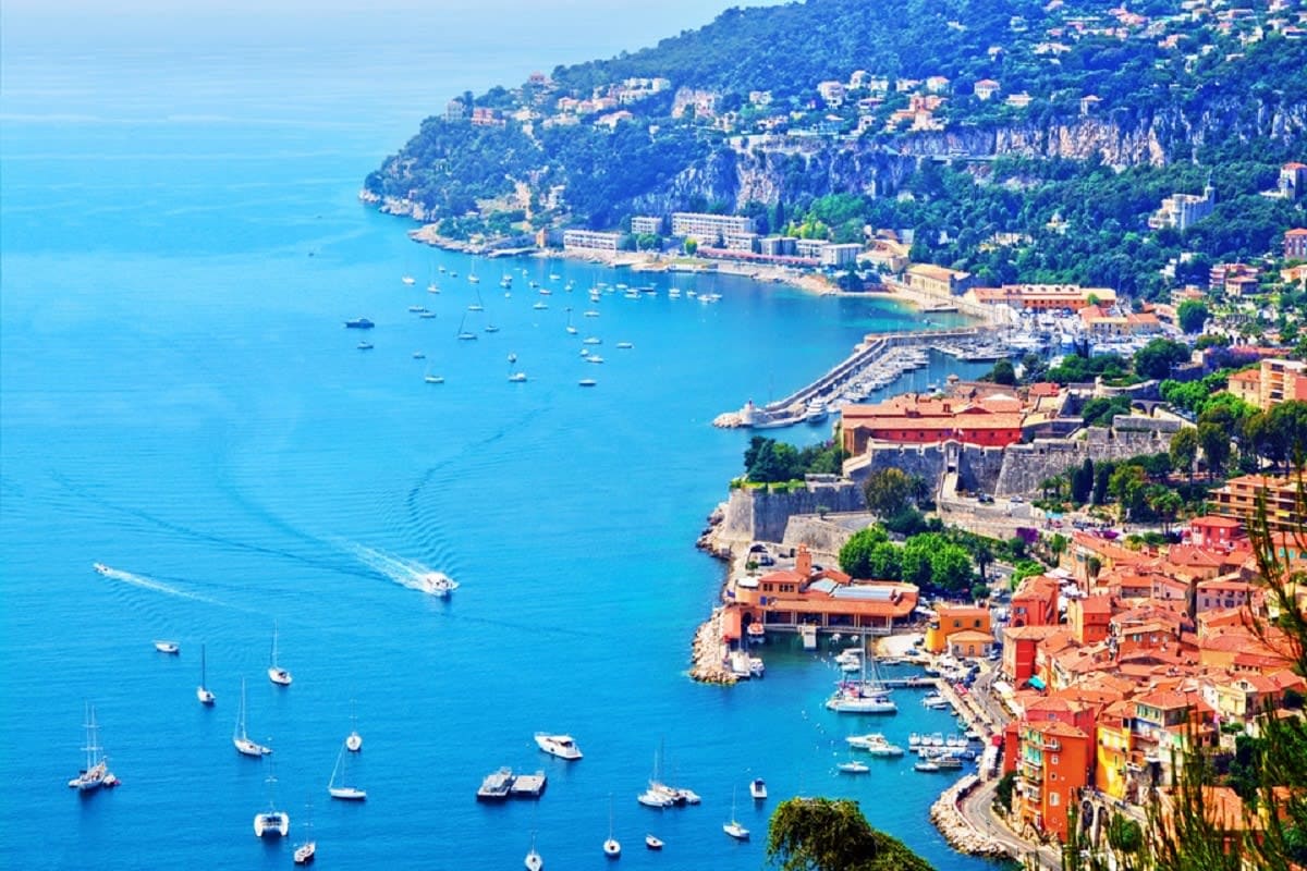 Aerial view of Villefranche-sur-Mer on the French Riviera with colorful buildings, sailboats in turquoise bay, and clifftop c