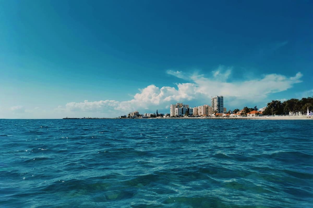 Coastal view of Larnaca, Cyprus beachfront with turquoise Mediterranean Sea, sandy beach, residential buildings, and clear bl