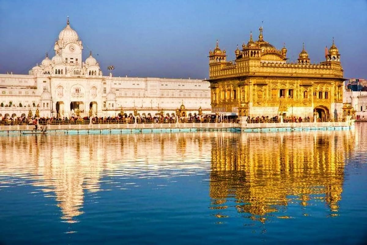 Golden Temple in Amritsar reflected in the sacred pool with white temple building and crowds of pilgrims