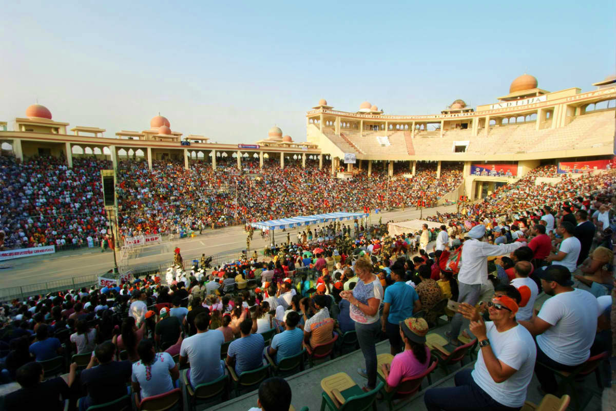 Packed stadium with thousands of spectators watching an event at a large ornate building with golden domes in India