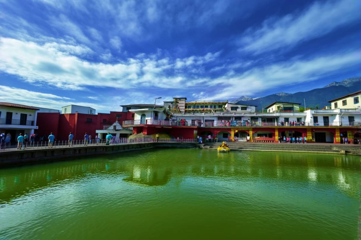 Colorful waterfront buildings and canal with visitors at a scenic tourist destination surrounded by mountains under blue sky