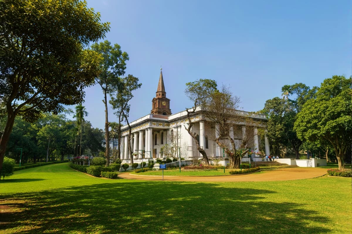 White colonial church with golden steeple surrounded by green lawns and tropical trees under clear blue sky