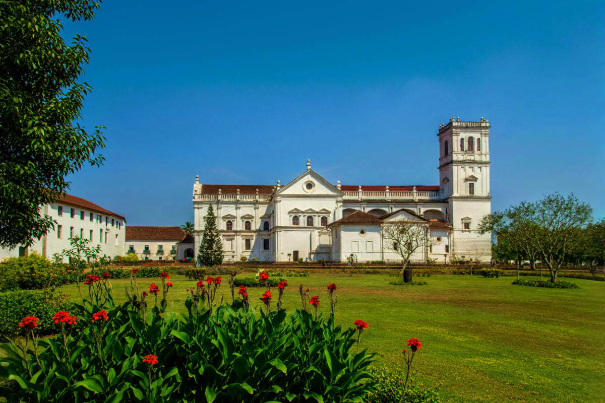 Historic white church with bell tower surrounded by green lawn and red flowers under clear blue sky in Himachal Pradesh