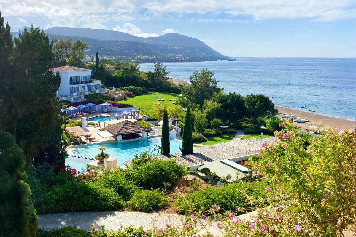 Luxury beachfront resort with swimming pools, manicured gardens, and Mediterranean Sea overlooking mountain coastline in Cypr