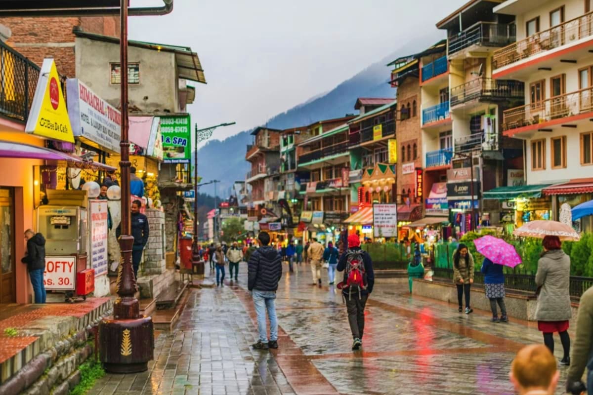 Wet street scene in a Himalayan mountain town with colorful buildings, shops, and tourists with umbrellas walking through the