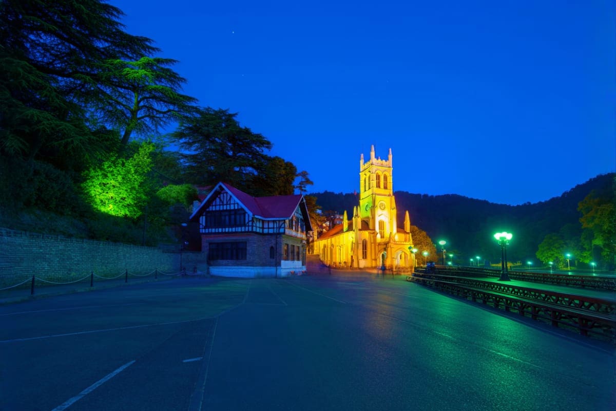 Illuminated Christ Church with colonial architecture at night in Shimla, surrounded by pine trees and green-lit pathways