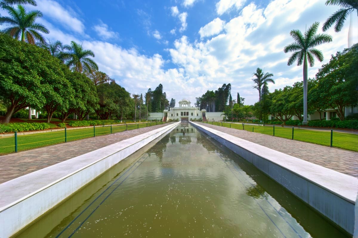 Symmetrical reflecting canal lined with white walls leading to white domed temple building with palm trees and green lawns un