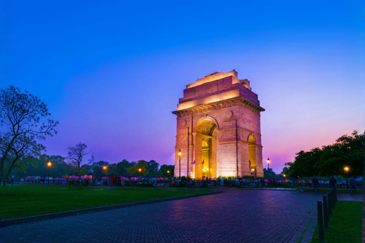 India Gate monument illuminated at dusk with crowds of visitors in New Delhi during twilight hours
