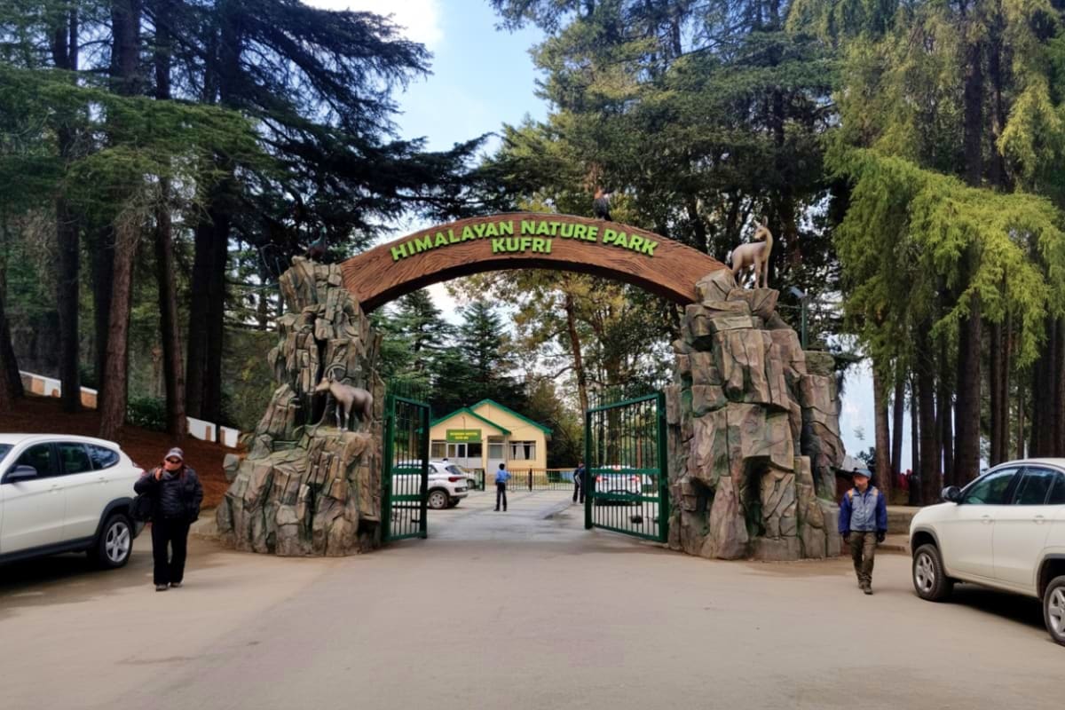 Entrance gate to Himalayan Nature Park Kufri with carved stone pillars, green metal gates, and visitor facilities nestled amo