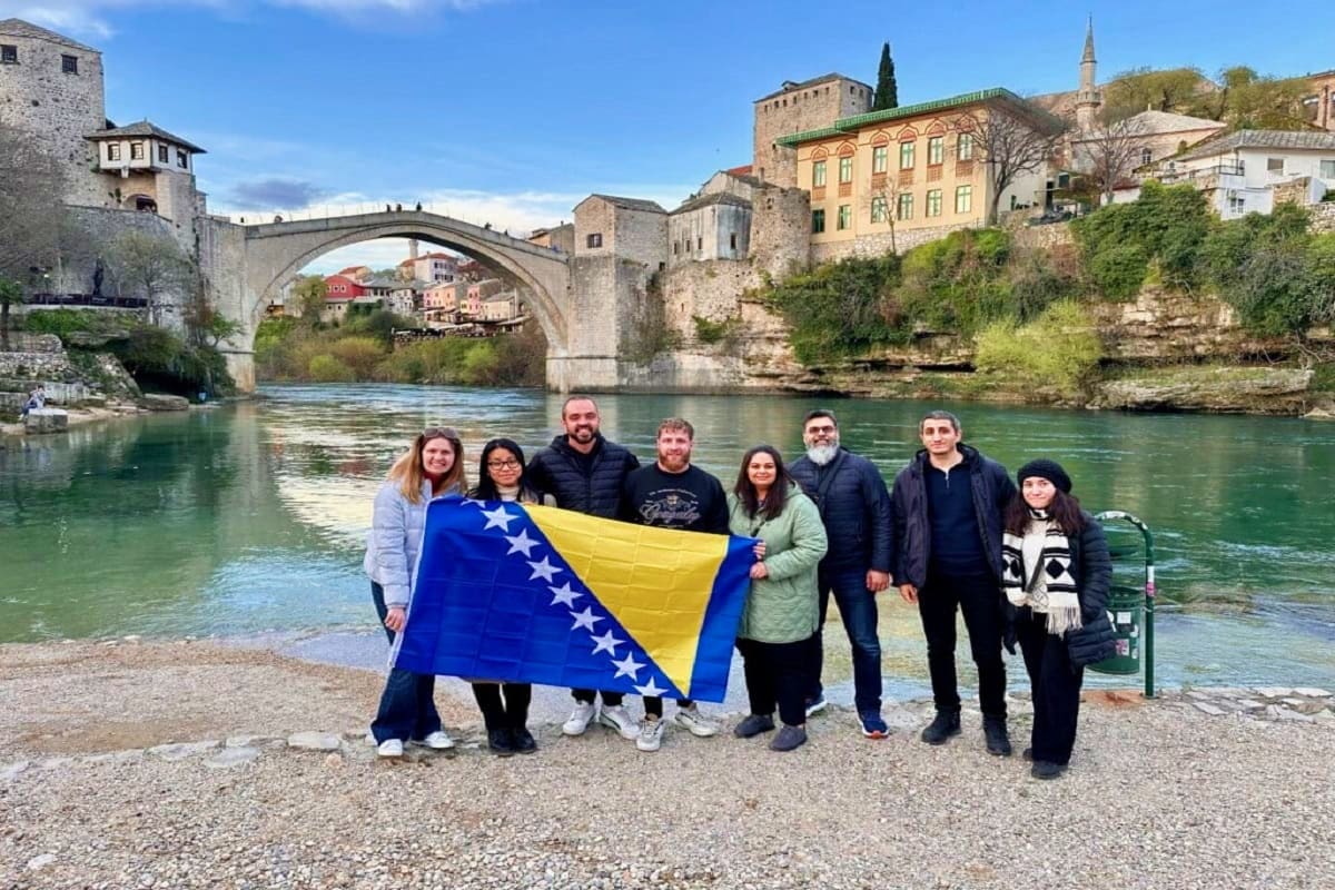 Explore Bosnia & Herzegovina Group of tourists holding Bosnia and Herzegovina flag at Stari Most bridge in Mostar with turquoise river and historic town b