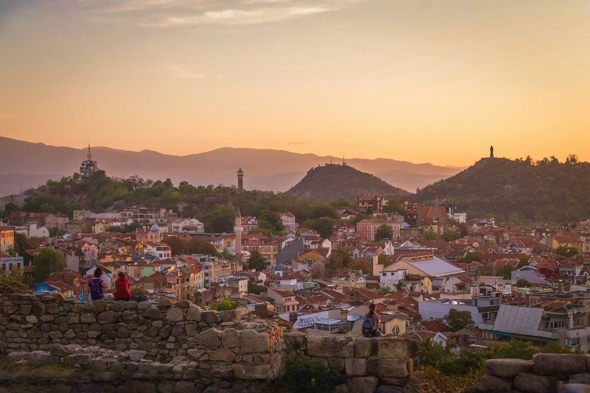 Sunset view of Plovdiv, Bulgaria cityscape with red-roofed buildings, historic churches, distant mountains, and ancient stone