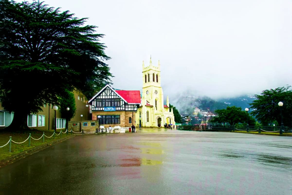 Christ Church in Shimla with yellow steeple, wet plaza, and misty Himalayan mountains in background