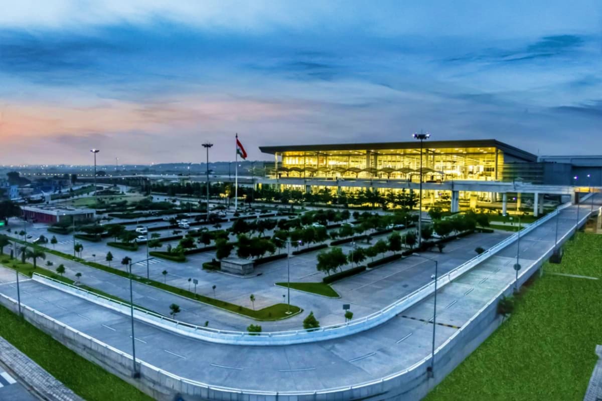 Modern illuminated building with landscaped parking area, curved roads, and flag at dusk