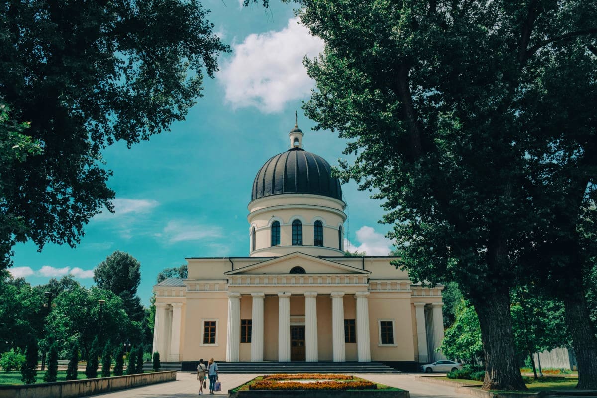Historic white neoclassical cathedral with black dome surrounded by tall trees and visitors in Moldova's capital city