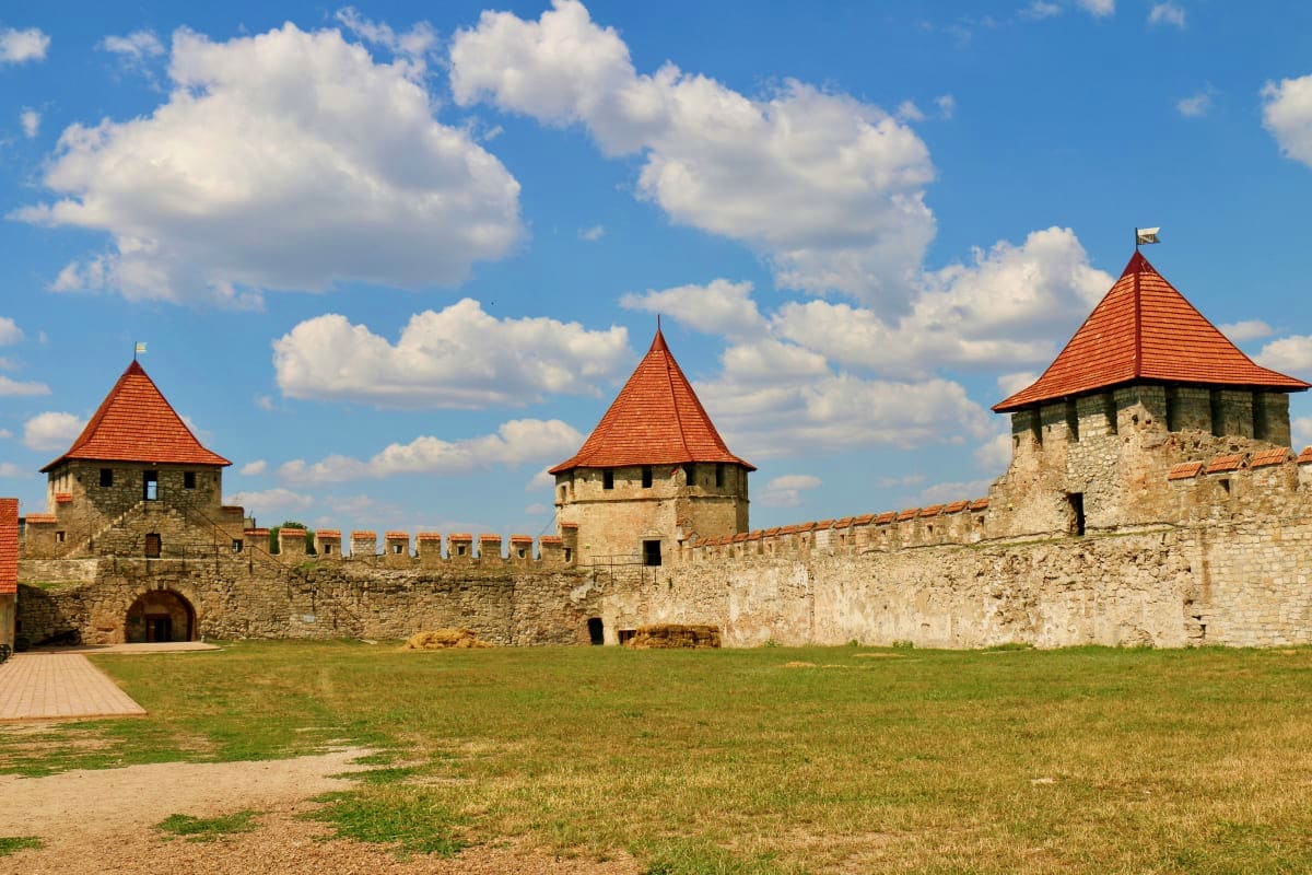 Medieval fortress with stone walls and three towers with red-tiled roofs under blue sky with white clouds in Moldova