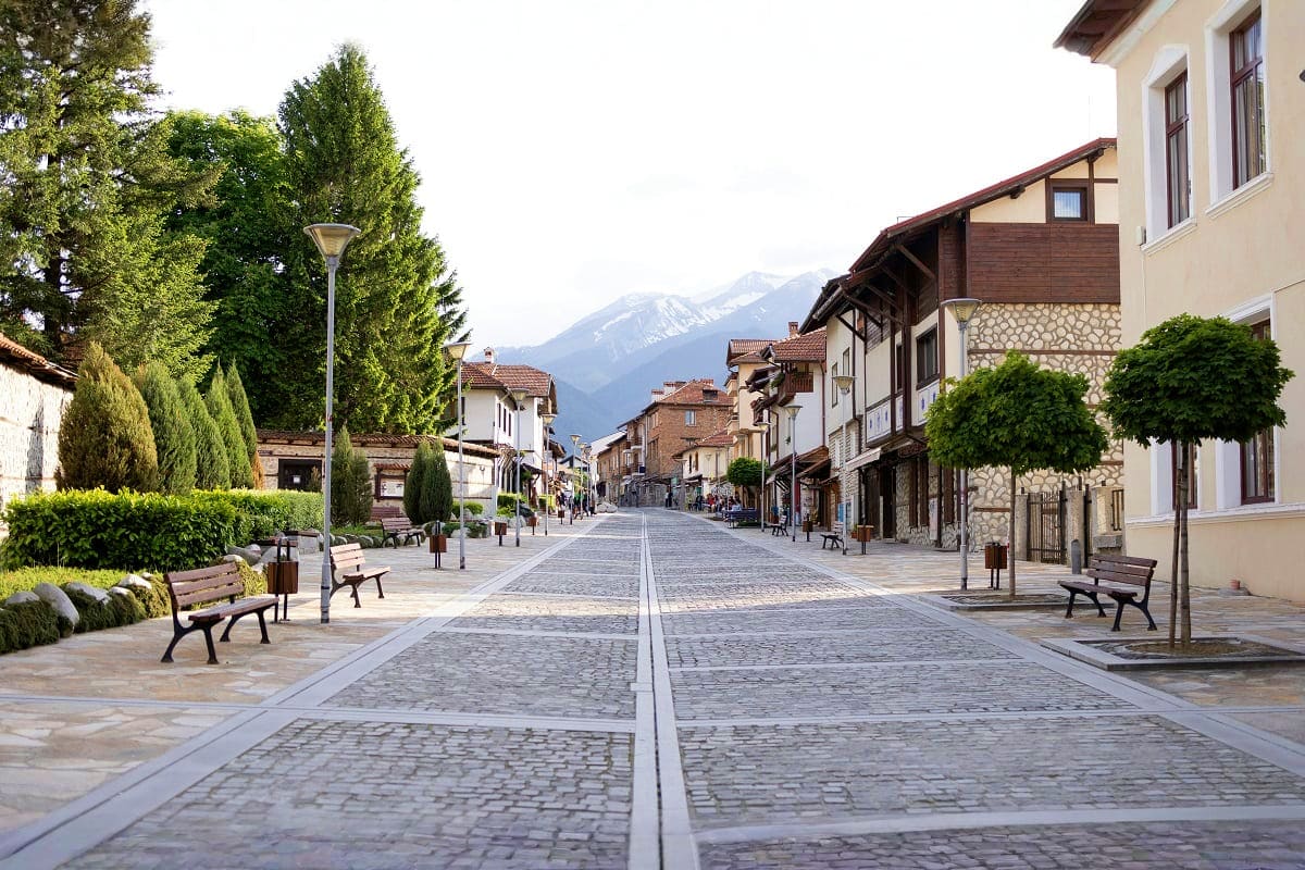Picturesque European town square with cobblestone street, traditional architecture, benches, and snow-capped mountain views i