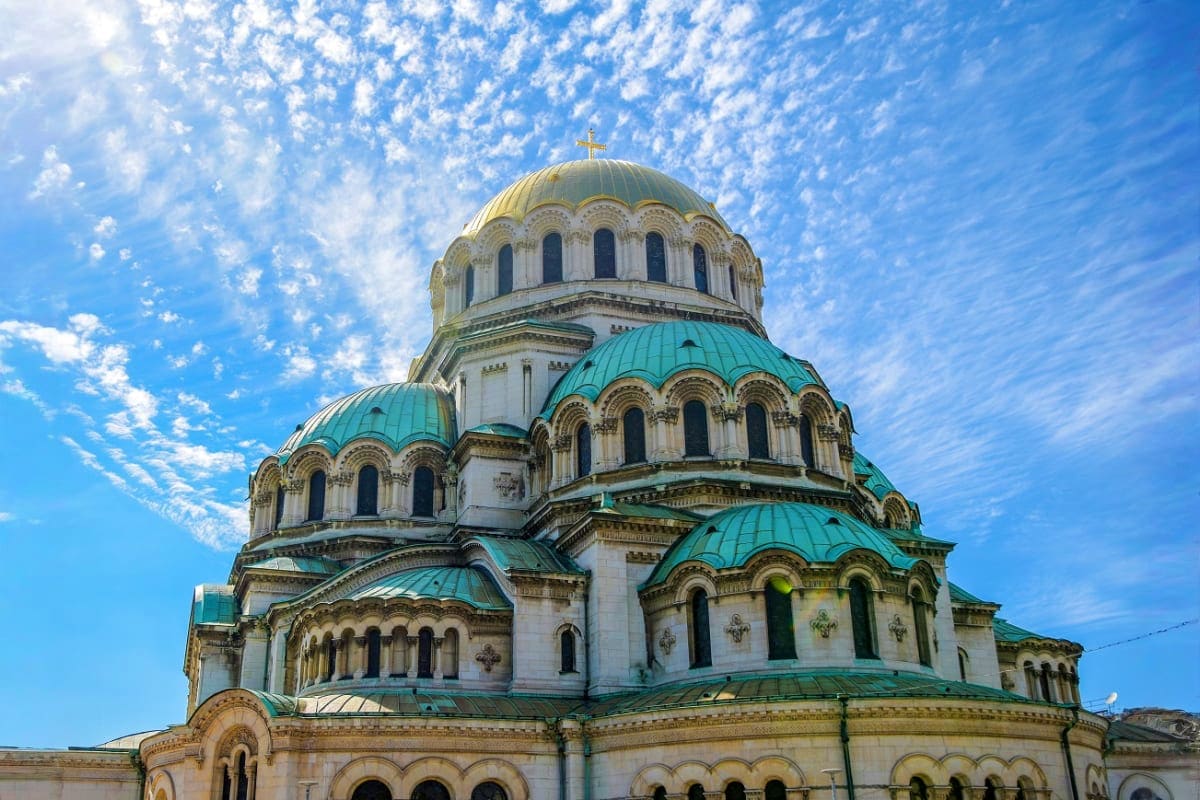 Alexander Nevsky Cathedral in Sofia, Bulgaria with golden dome and turquoise copper roofs against blue sky with white clouds
