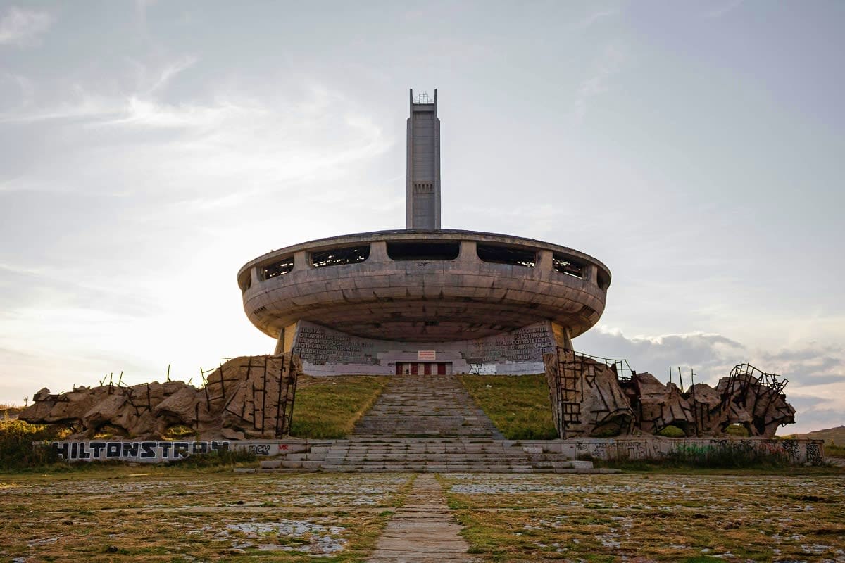 Abandoned futuristic concrete monument with circular disk structure and central tower in Bulgarian mountains