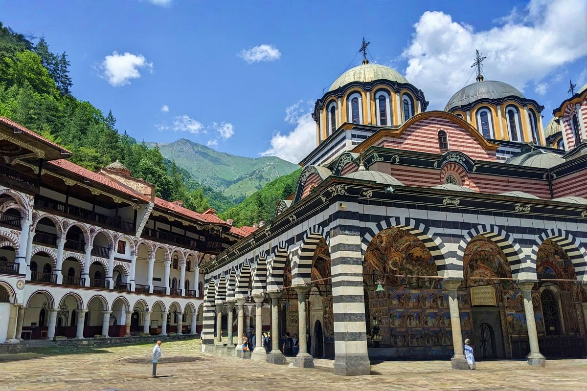 Rila Monastery courtyard with Byzantine domed church featuring golden cupolas and striped stone archways, surrounded by mount