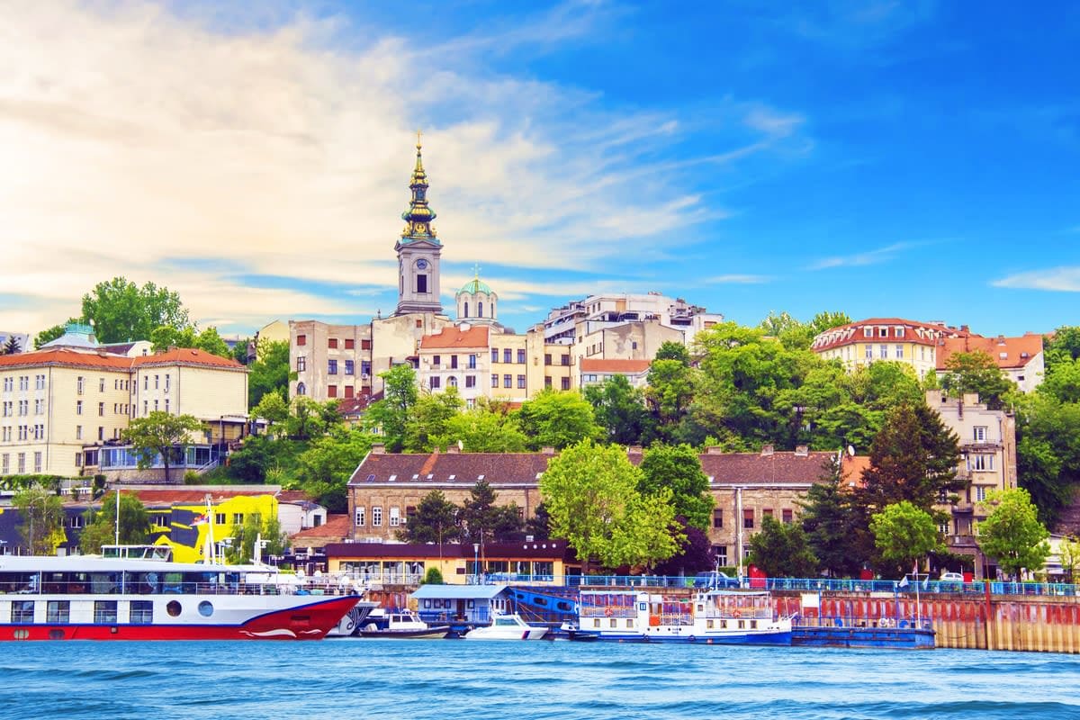Danube River waterfront view of Belgrade's Zemun district with colorful riverside boats, historic Orthodox church tower, and 