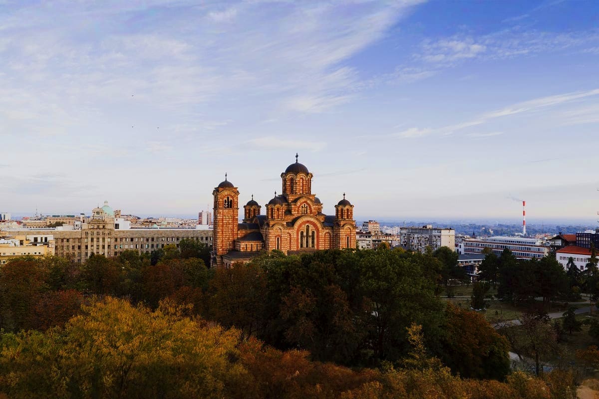 Church of Saint Sava with golden domes overlooking Belgrade cityscape and Danube River surrounded by autumn trees
