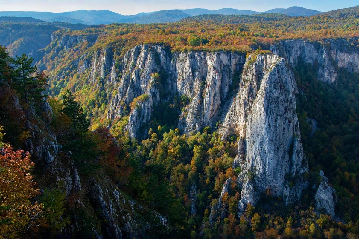 Dramatic limestone cliffs and forested valleys in Serbia's Plitvice Lakes region during autumn, showcasing towering rock form