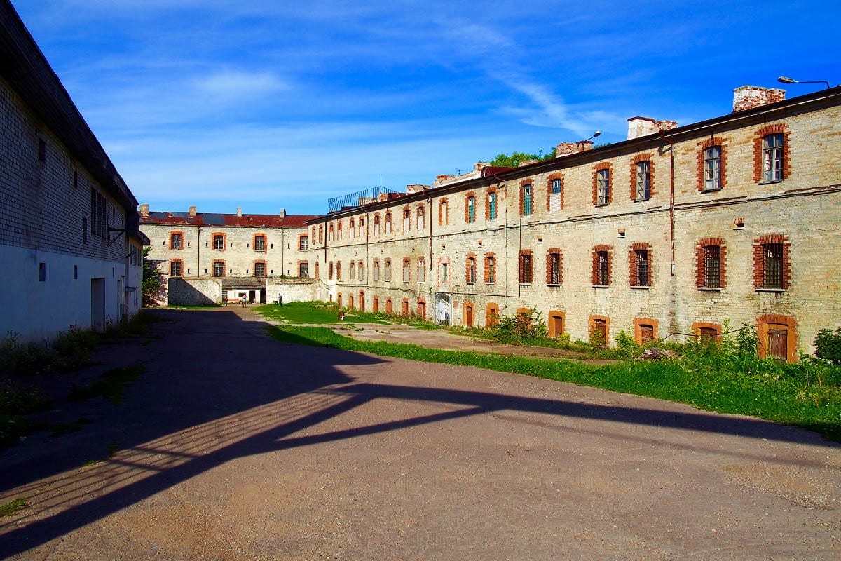 Historic stone prison courtyard with multi-story barred windows and green grounds under blue sky in Tallinn, Estonia