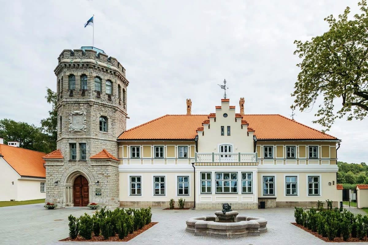 Historic stone tower and white manor house with orange roof and courtyard fountain in Tallinn, Estonia
