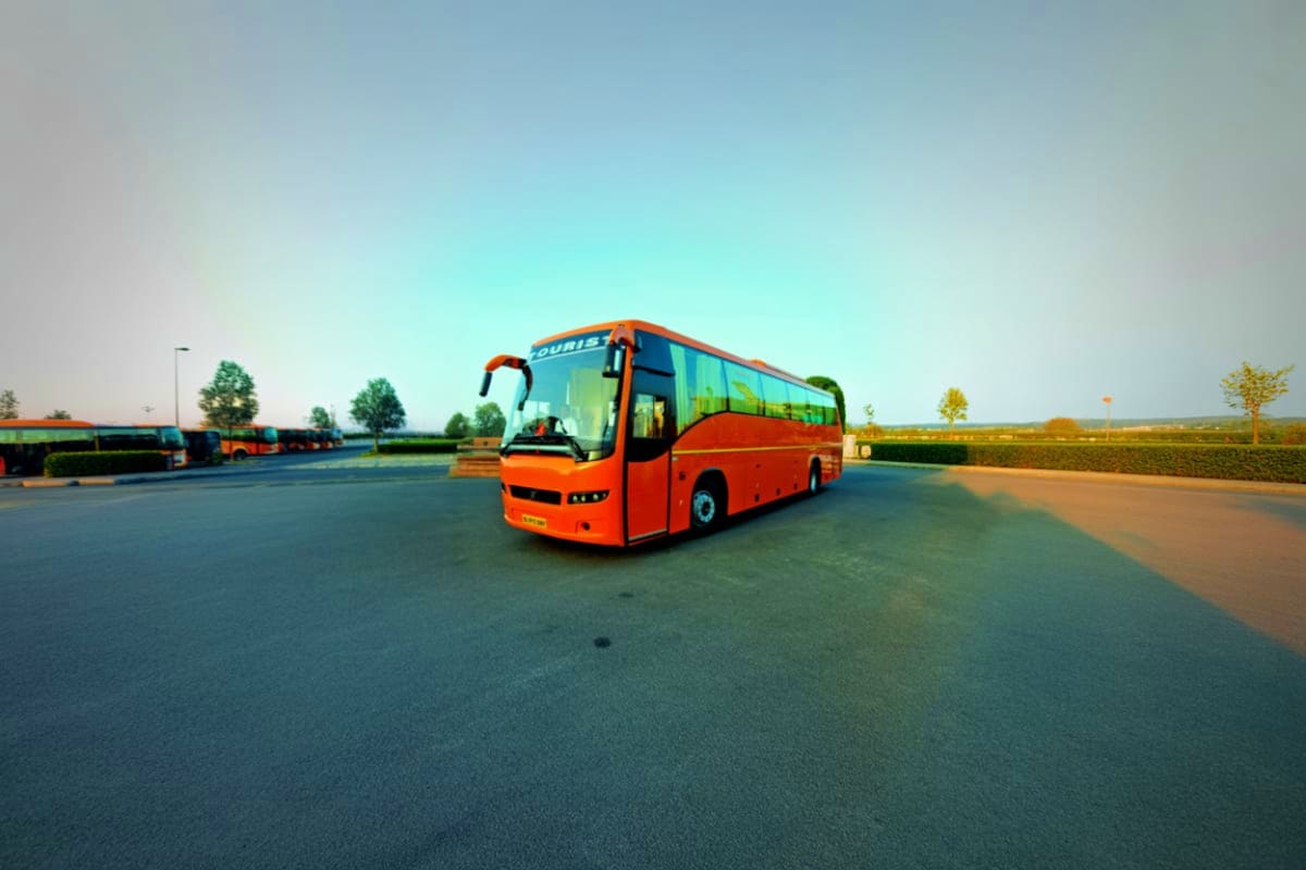 Red and orange Volvo tour bus parked on empty asphalt road with clear sky and green fields in background
