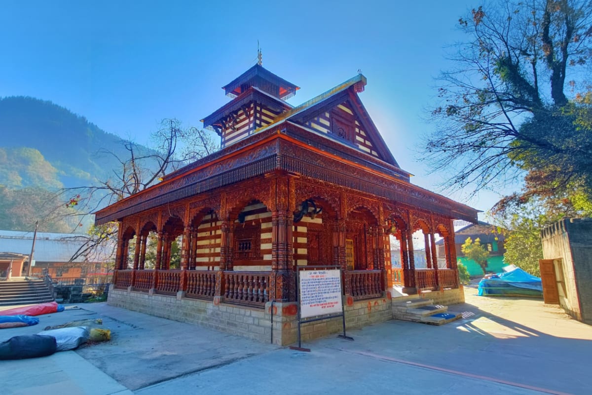 Traditional Himalayan temple with ornate wooden architecture and tiered pagoda roof overlooking mountain lake in Manali
