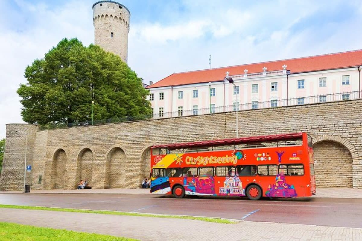 Red double-decker tour bus in front of Toompea Castle with medieval tower and fortification walls in Tallinn, Estonia
