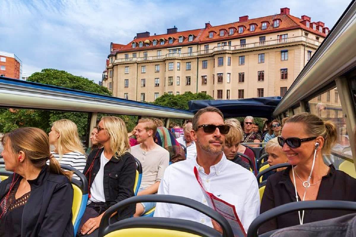 Tourists on an open-top bus tour with a historic Scandinavian apartment building featuring mansard roof in the background