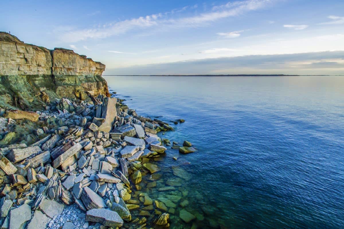 Dramatic rocky cliff coastline with hexagonal basalt columns overlooking calm blue sea and distant horizon under clear sky