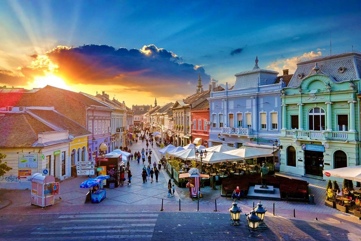Colorful historic buildings and outdoor market at sunset in a European town square with pedestrians and white market umbrella