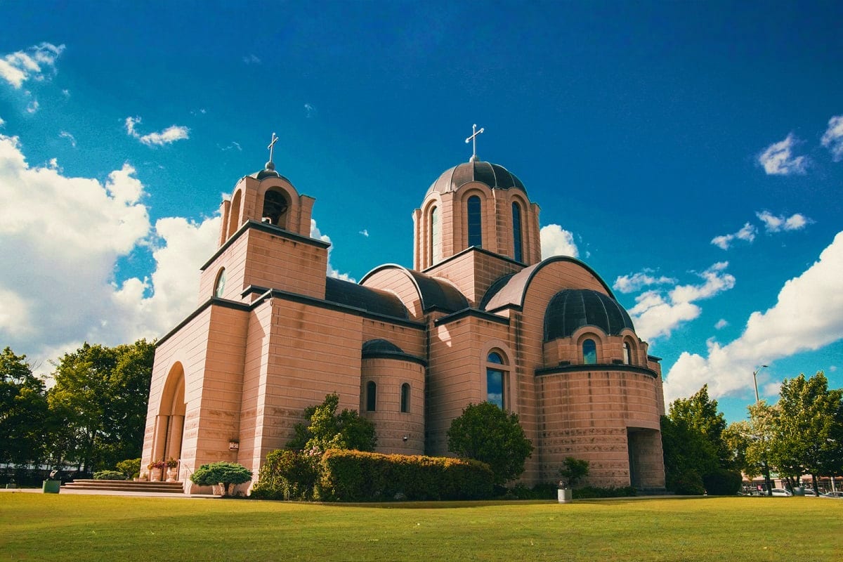 Modern Orthodox church with distinctive domed architecture and crosses, surrounded by green lawn and trees under blue sky