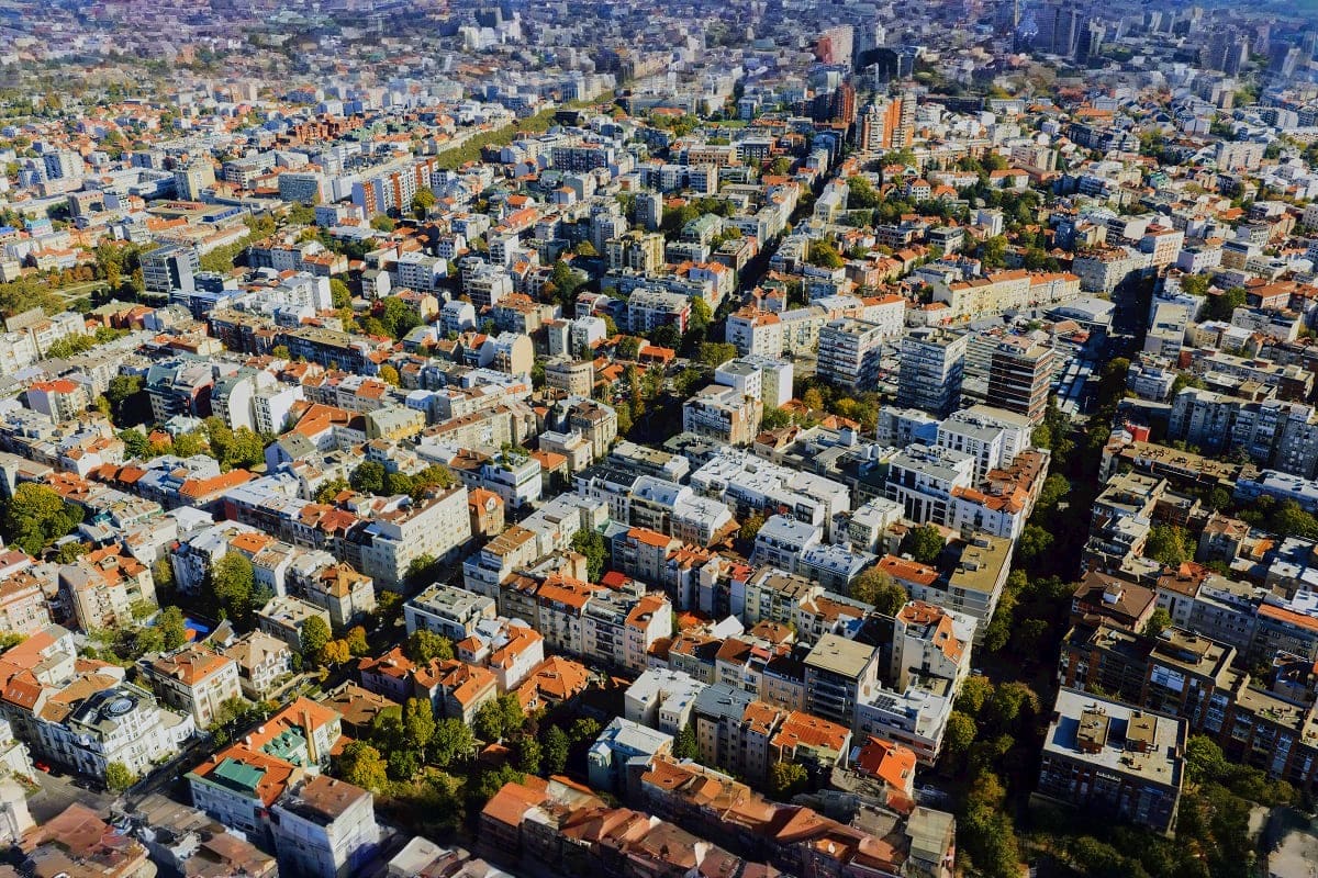 Aerial view of Belgrade cityscape showing dense residential neighborhoods with terracotta roofs, modern apartment buildings, 