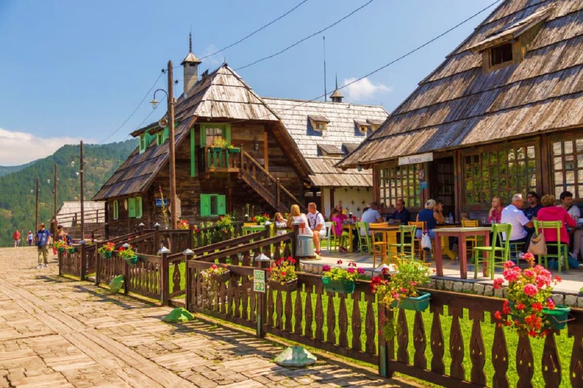 Traditional wooden village houses with thatched roofs, colorful green fences and red flowers in a mountain valley settlement 