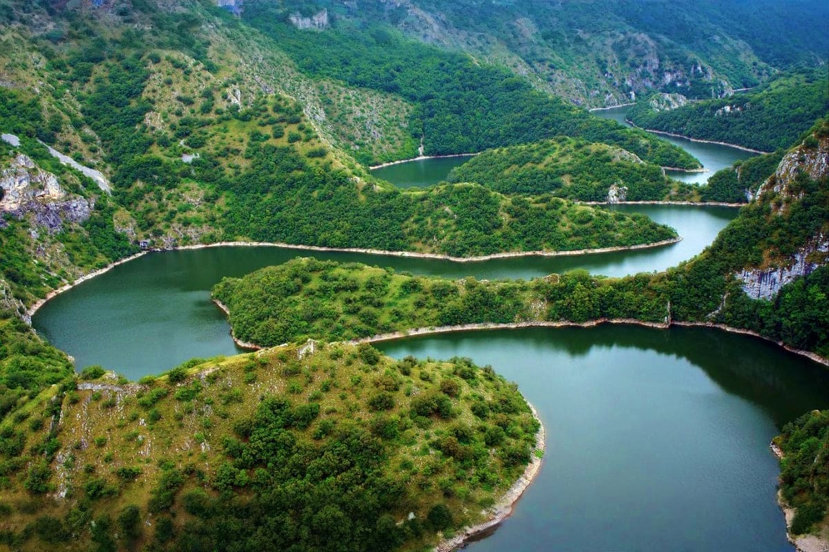 Aerial view of Meanders of Drina river with turquoise water winding through green forested mountains and limestone cliffs in 