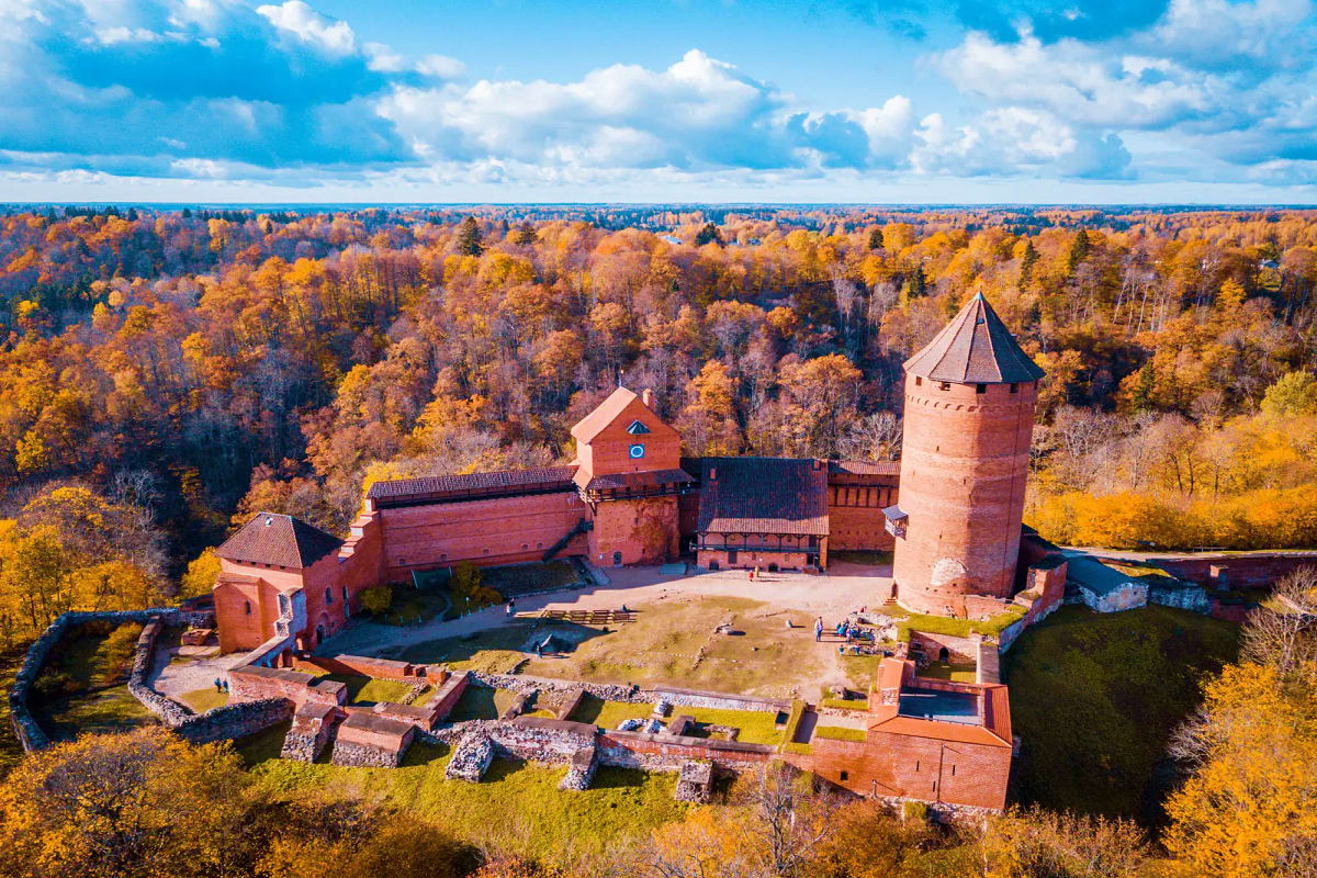 Aerial view of Trakai Island Castle with red brick towers surrounded by autumn forest and blue sky in Lithuania