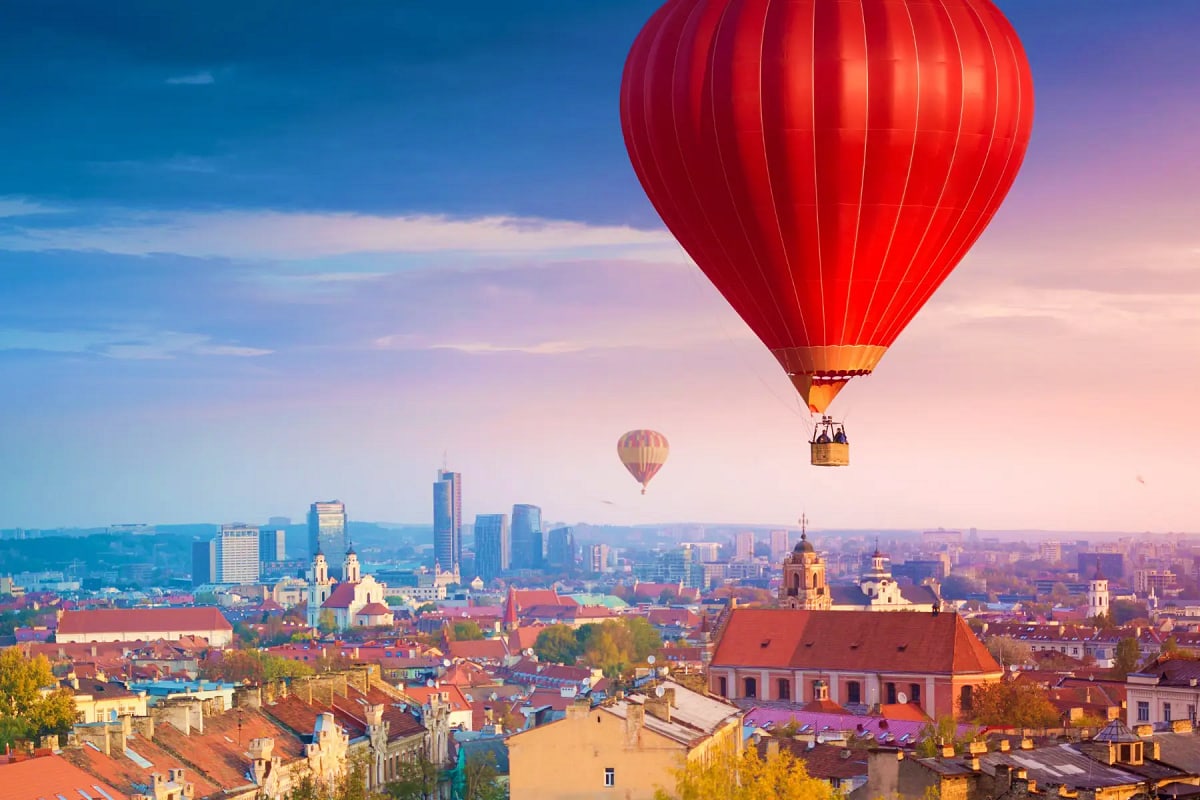 Red hot air balloon floating above historic European city with churches and medieval architecture at sunrise