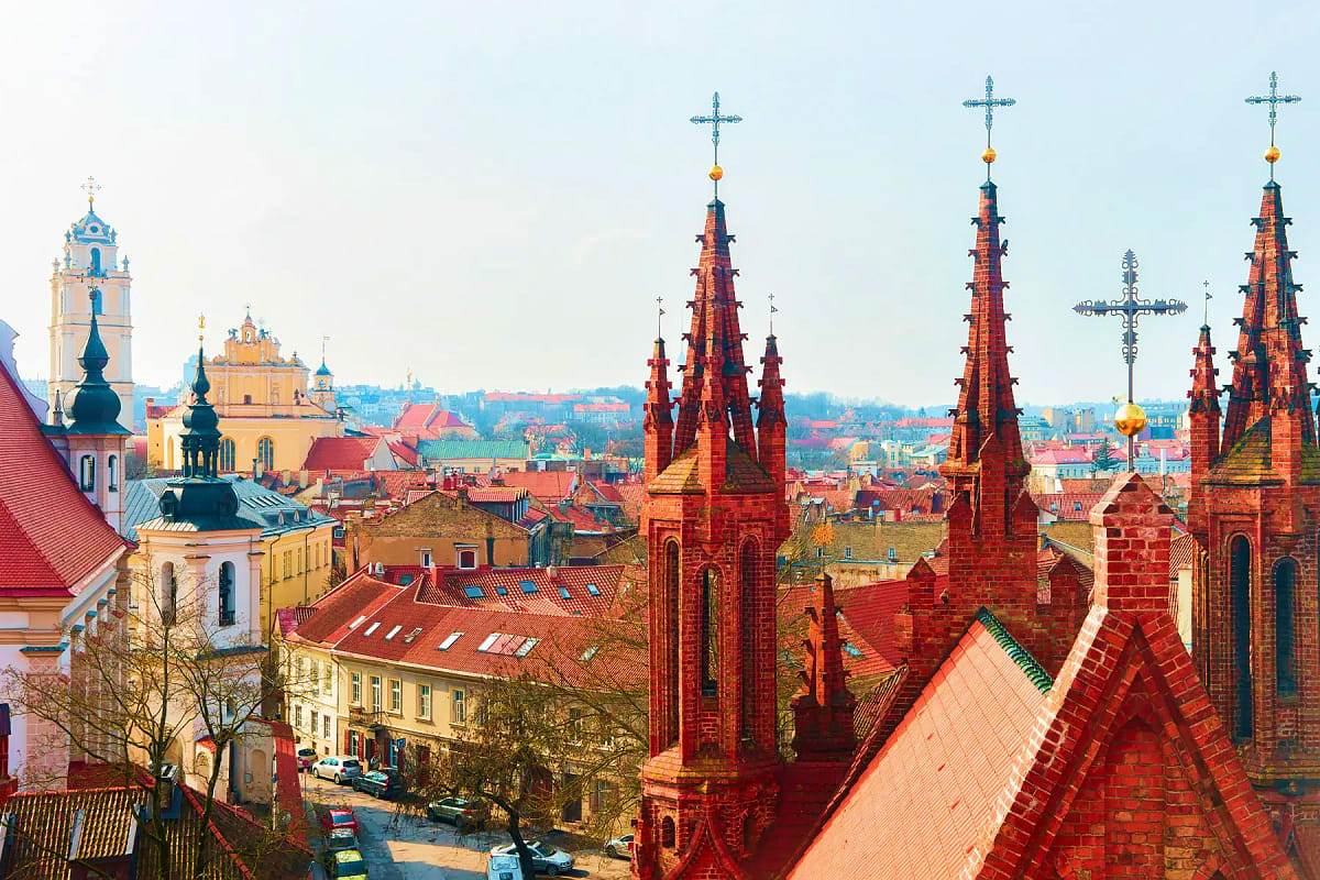 Aerial view of historic European cityscape with red brick churches, ornate steeples with golden crosses, and traditional arch
