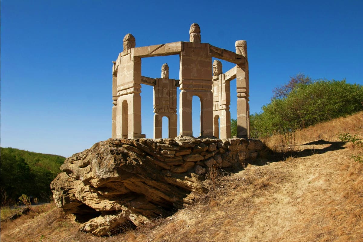 Ancient stone gateway with carved eagle finials standing on rocky outcrop under clear blue sky in Moldova countryside