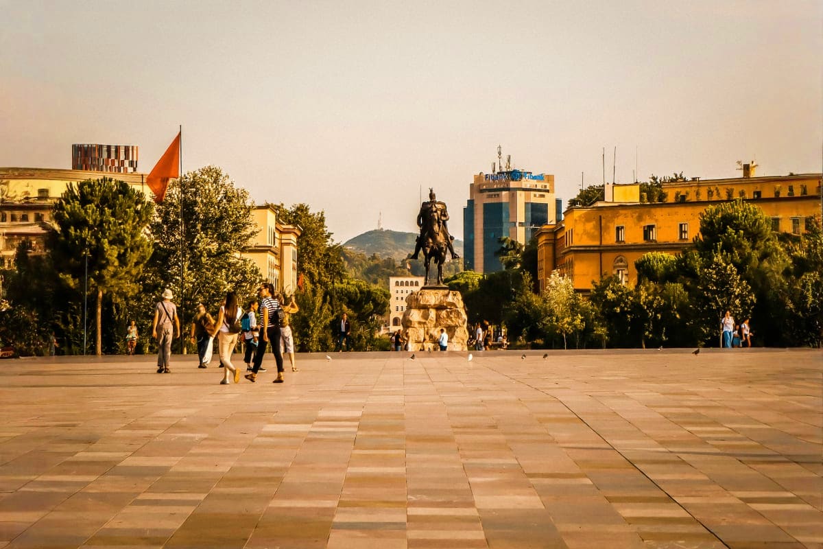 Skanderbeg Square in Tirana, Albania with equestrian statue, surrounding yellow buildings, trees, and visitors in the plaza