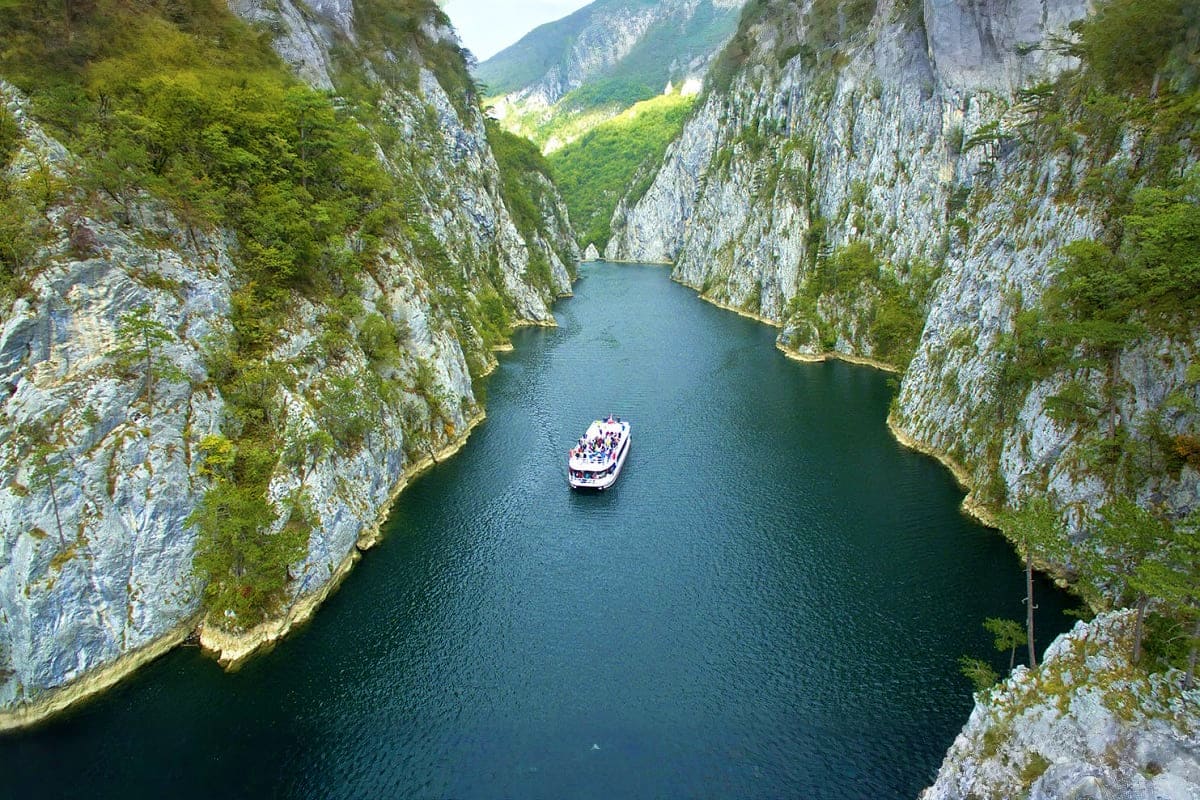 Tourist boat navigating through a dramatic limestone gorge with steep white cliffs and green vegetation in Serbia