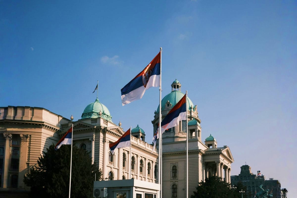 Serbian national flags flying in front of historic government buildings with green copper domes in Belgrade