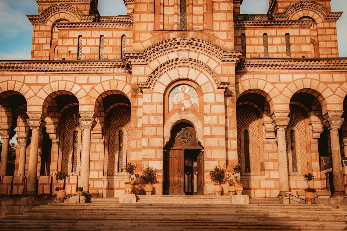 Historic red brick Byzantine church facade with ornate arches, columns, and religious mosaic in Serbia