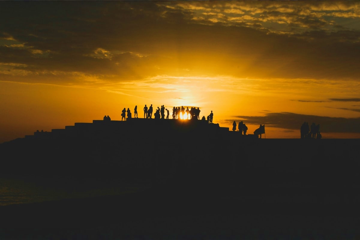 Silhouetted group of tourists standing on Ksamil fortress at sunset in Albania with golden sky and sun on horizon