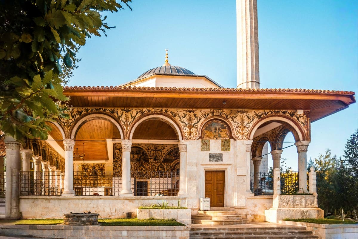 Ottoman-style mosque with ornate arches, dome, and minaret against clear blue sky, showcasing traditional Islamic architectur